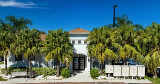 A white building with a brown roof is surrounded by palm trees.