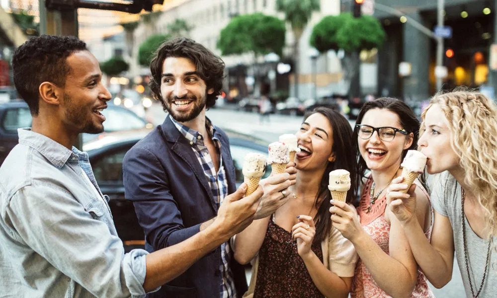 group of people eating ice cream on sidewalk on busy downtown street