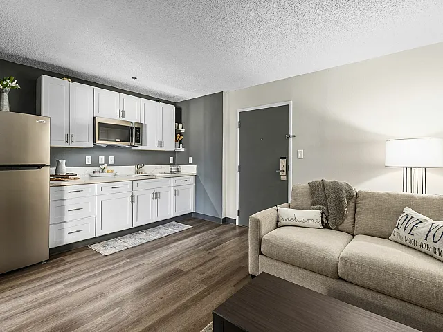 open living area with furniture next to a kitchen with white cabinetry