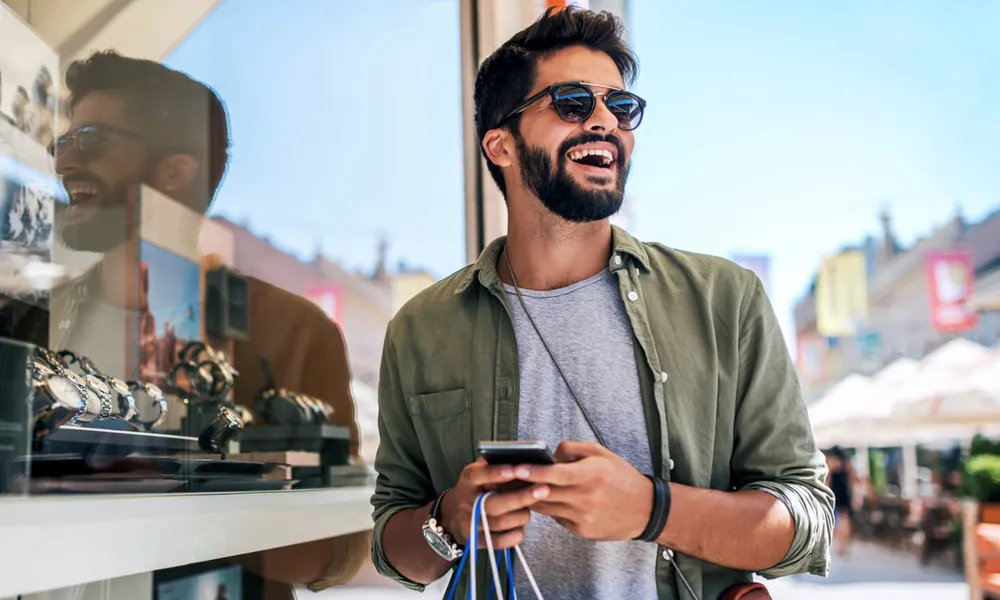 man with shopping bags and phone outside store selling watches on sunny day
