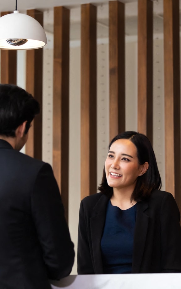 a woman smiling at a counter while talking to a man in front of a mirror