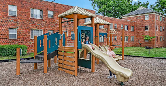 a child playing on a playground in front of a brick building at Hamilton Manor Apartments, Hyattsville, MD 20782