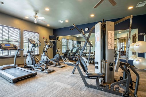 gym with lifting and cardio equipment with a big mirror and windows