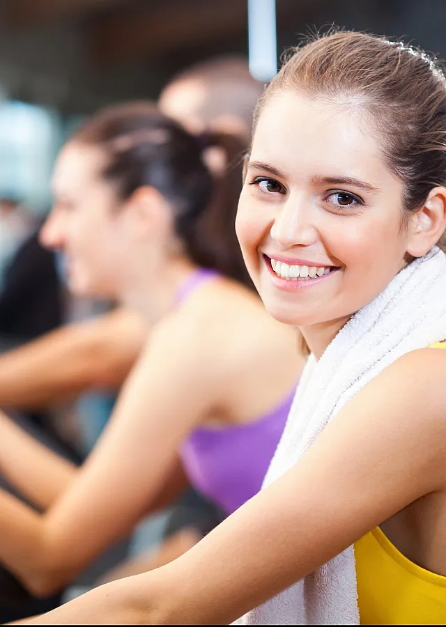 Energetic fitness setting with smiling individuals on exercise bikes, exemplifying a lively and motivating gym atmosphere.