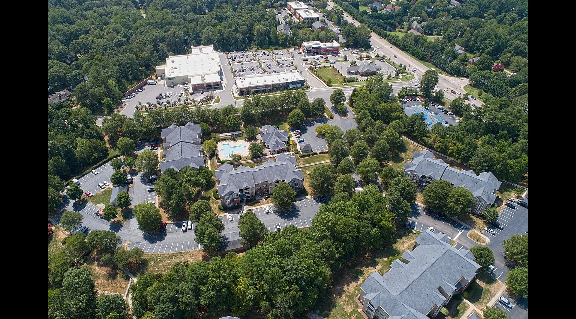 Vibrant aerial view showcasing beautiful apartment complex with scenic greenery, pristine swimming pool, and nearby shopping center.