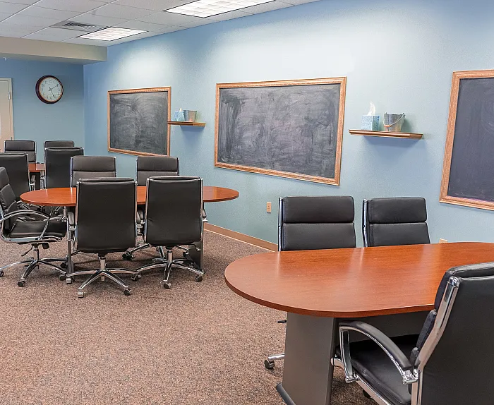 Modern and spacious conference room with sleek black chairs, oval wooden tables, and classic chalkboards for versatile presentations.