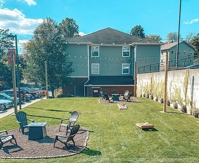 Charming apartment patio with lush green lawn, outdoor seating, and cozy fire pits under a clear blue sky.