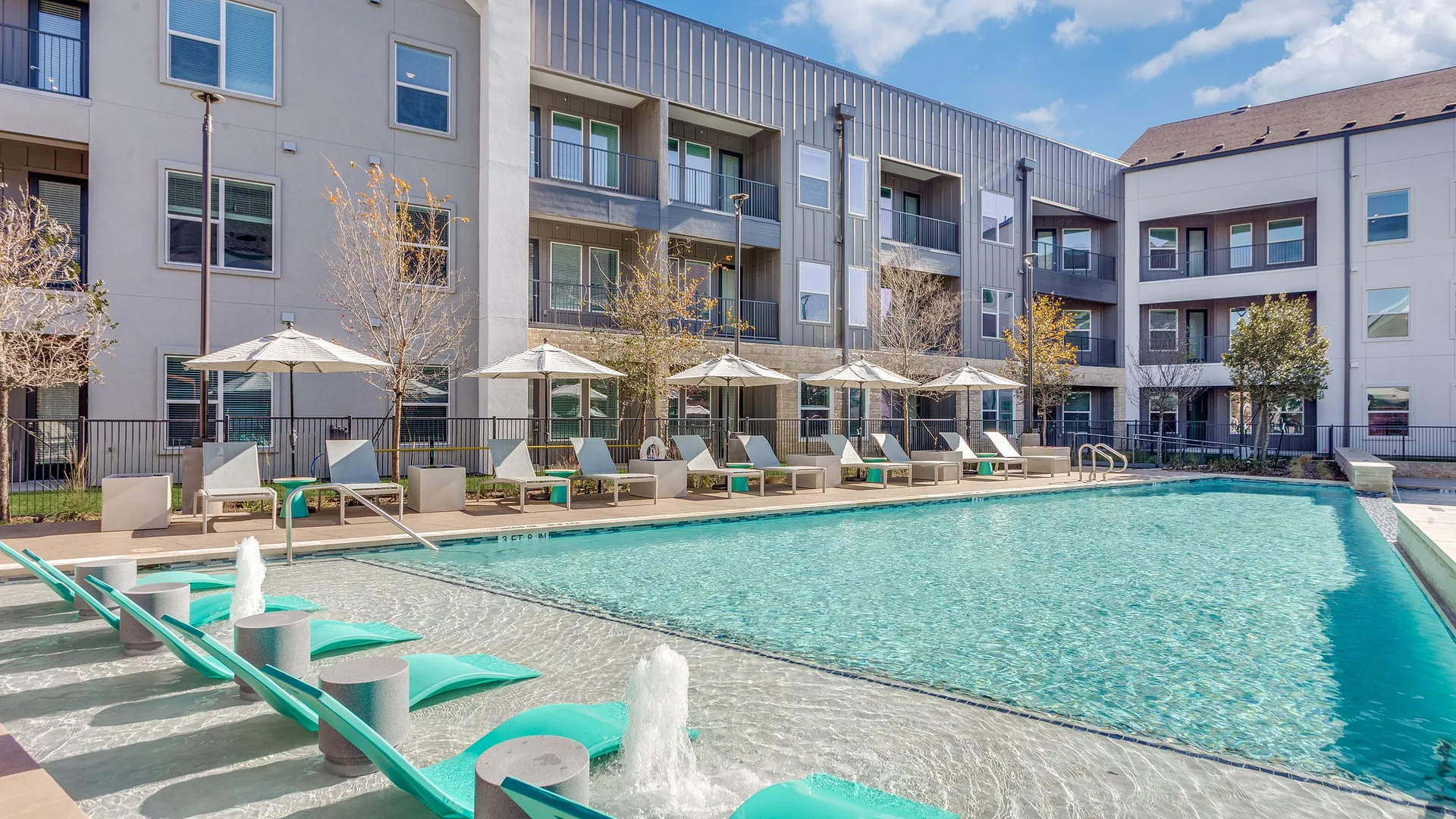 A sunny pool area with loungers and modern apartment buildings in the background.