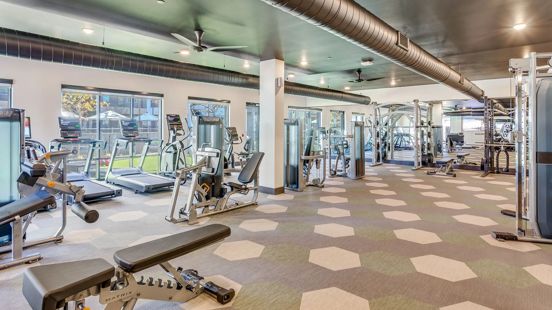 A modern gym with various exercise equipment and large windows for natural light.