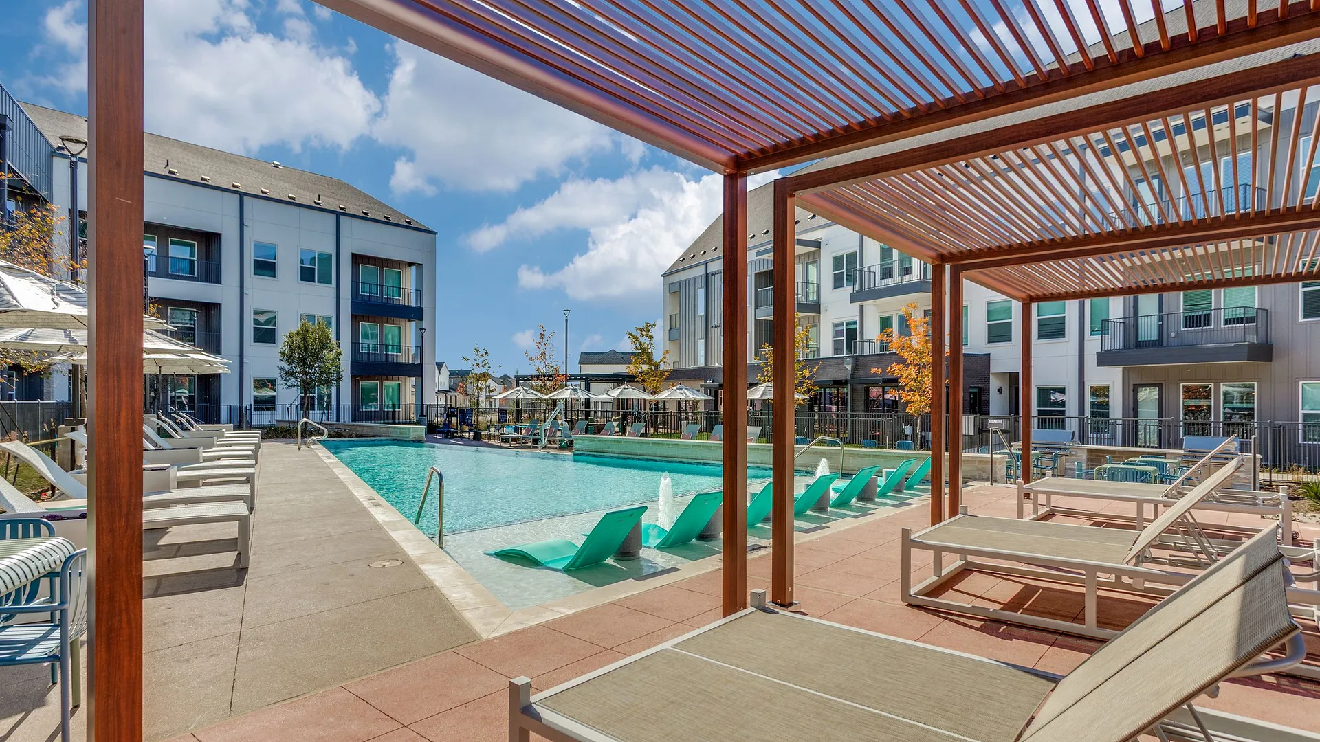 A modern apartment complex featuring a pool area with lounge chairs and canopies.