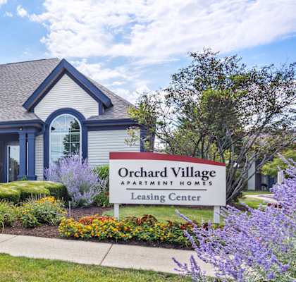 A blue and white house with a sign that says Orchard Village Apartment Homes.