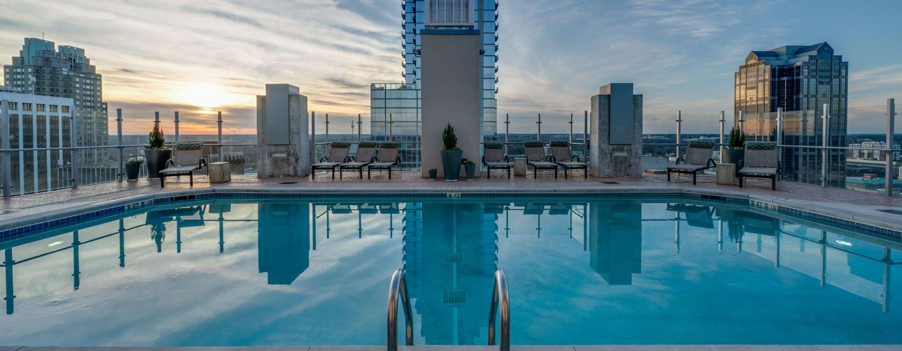 The rooftop pool lounge at Skyhouse Raleigh apartments in Raleigh, NC, featuring beach chairs and a view of the city.