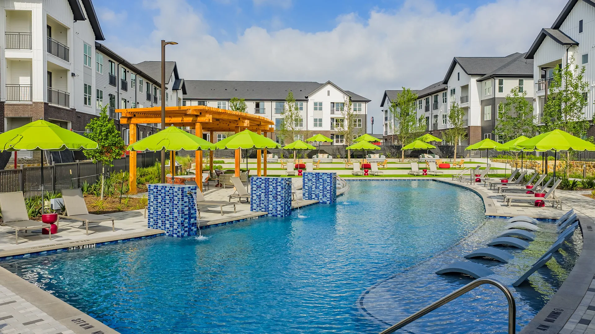A modern apartment complex featuring a vibrant outdoor pool area with lounge chairs and umbrellas.