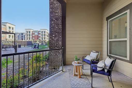 A balcony with a blue chair and a small table with a plant on it.