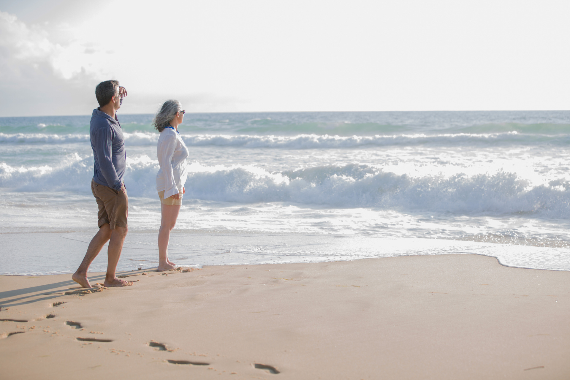 Couple walking barefoot along a sandy beach with ocean waves