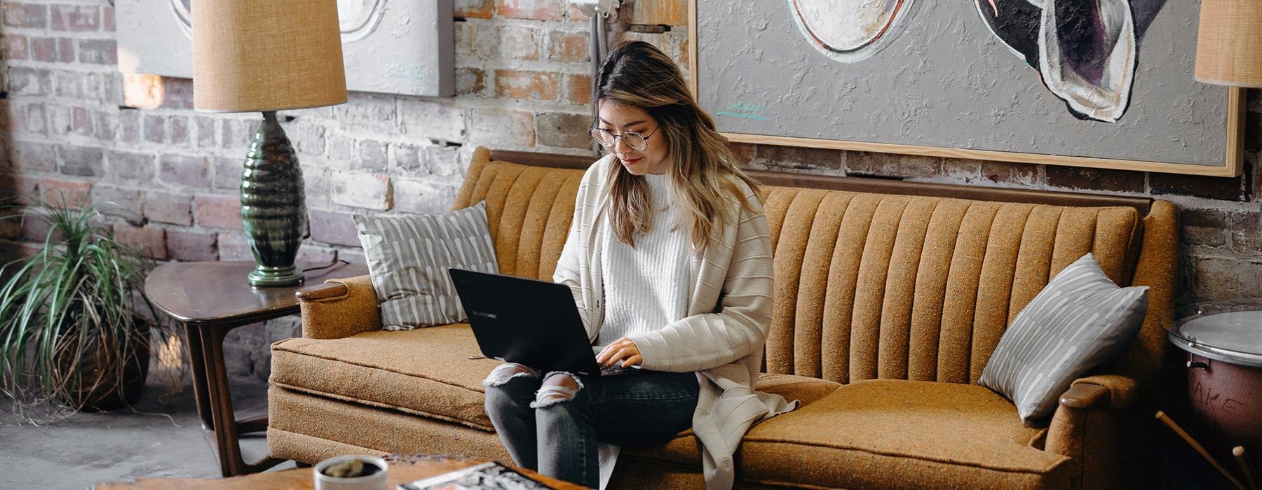 woman sits on a couch using a laptop in cafe