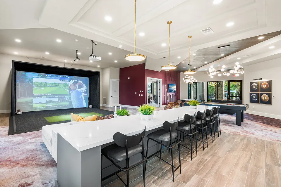 Luxurious entertainment space featuring a golf simulator, elegant bar seating, chic lighting fixtures, and a pool table for ultimate relaxation.