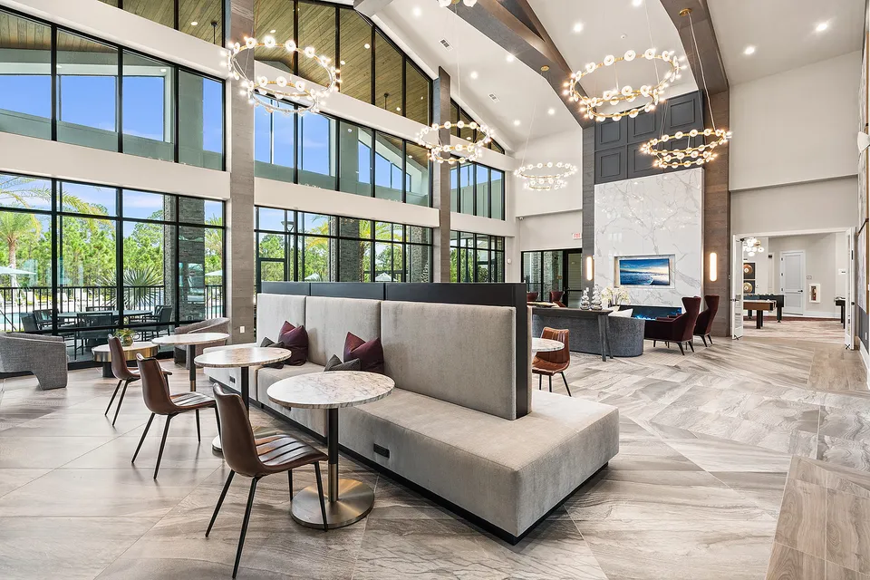 Elegant and modern lounge area with high ceilings, large windows, stylish chandeliers, and chic seating, offering a bright and inviting space.