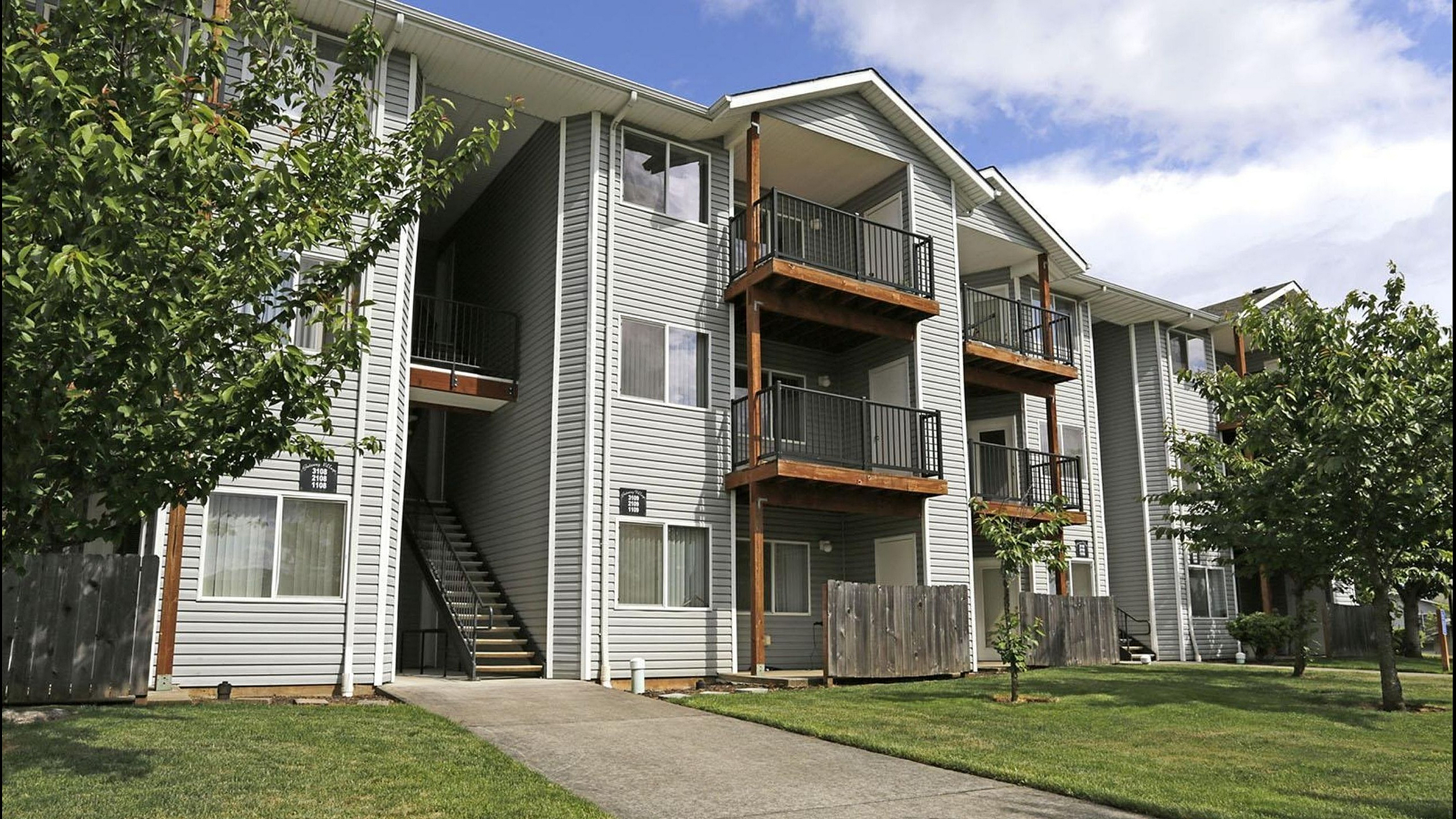 Charming multi-story apartment building with private balconies, surrounded by lush greenery and a serene pathway.