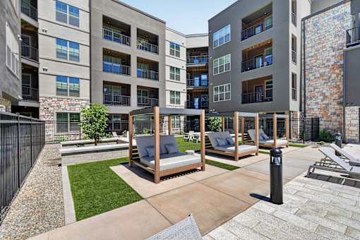 A modern outdoor seating area with a wooden swing set and a stone wall.