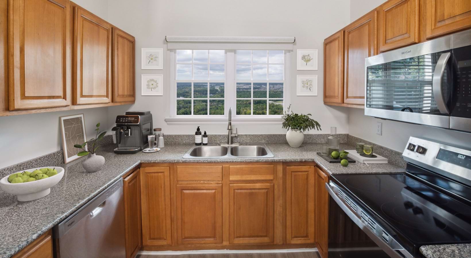 1 Bedroom Apartments in Leland, NC - Flats at Leland - a Kitchen with Spacious Granite Countertops, Stainless Steel Appliances Including an Oven, Dishwasher, and Built-In Microwave, Brown Wood-Style Cabinetry, and a Window Above the Sink