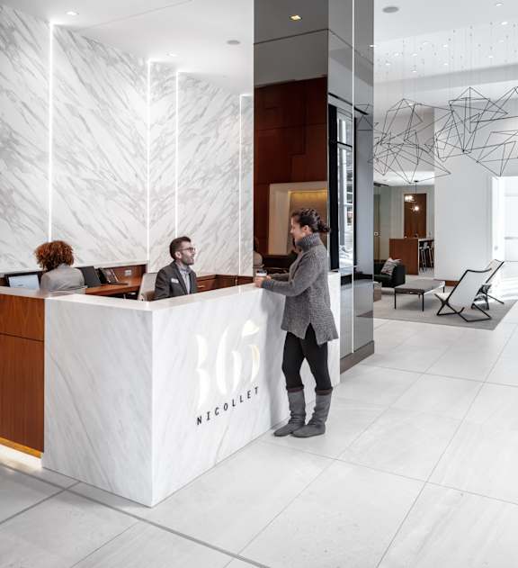 A reception area with a white reception desk and two people behind it at 365 Nicollet, Manchester , 55401
