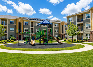 A playground with a green slide and a blue canopy is surrounded by apartment buildings.
