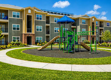 A playground with a green slide and a blue canopy is in front of a multi-story apartment building.