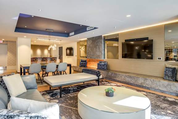 A modern living room with a grey sofa, a round white table, and a TV mounted on the wall.