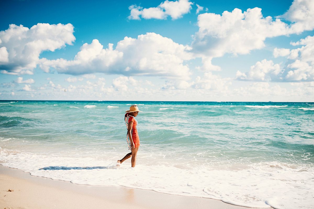 Girl with hat dressed in red getting her feet wet at the beach.