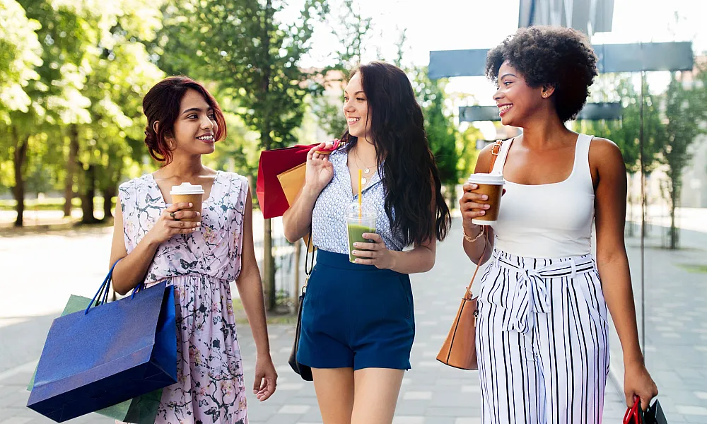 three women walking outdoors with shopping bags and smoothies