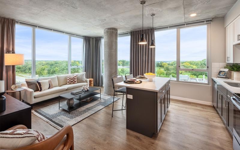 a living room with a kitchen and large windows