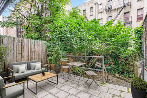 A patio with a table and chairs surrounded by green plants.