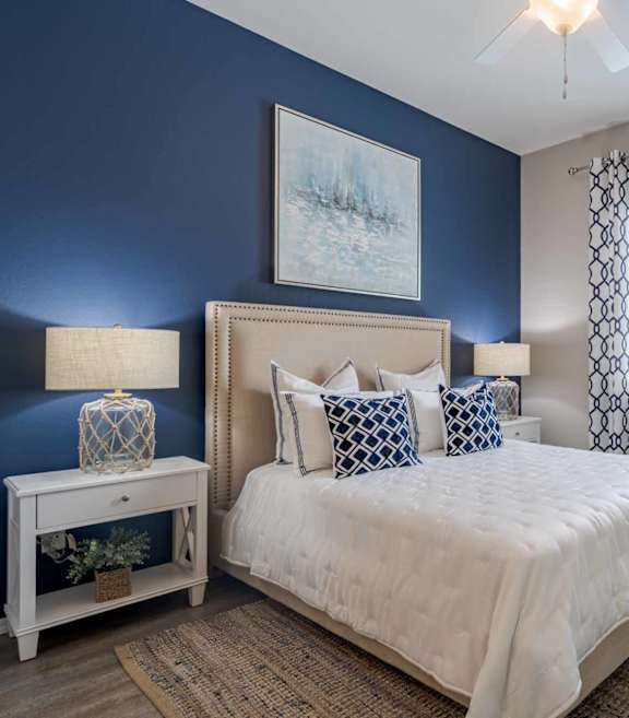 A bedroom with a bed, nightstand, and a plant. at Vistoria At Stadium Apartments, Glendale, Arizona