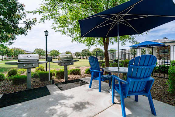 A blue chair is in front of a table with a blue umbrella. at Vistoria At Stadium Apartments, Glendale, Arizona
