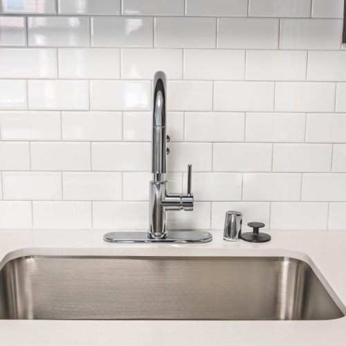 a kitchen sink with a white tiled wall behind it