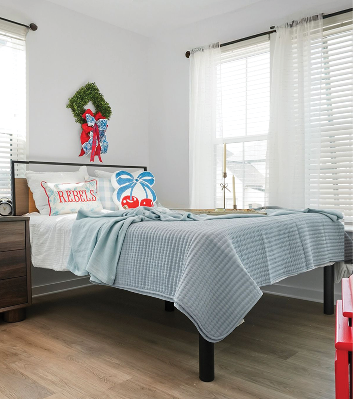 Cozy bedroom with festive decor, featuring a bed with blue bedding and a colorful wreath on the wall.