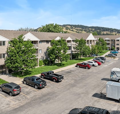 A parking lot with cars and a truck in front of apartment buildings.