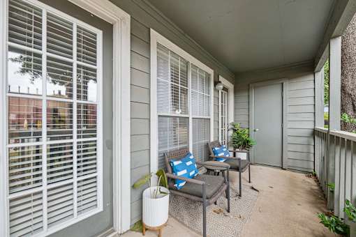 A patio with a couch, pillows, and a potted plant.