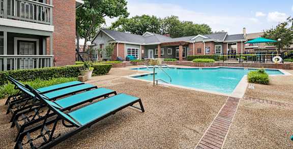 A pool surrounded by a brick building and a green lawn.