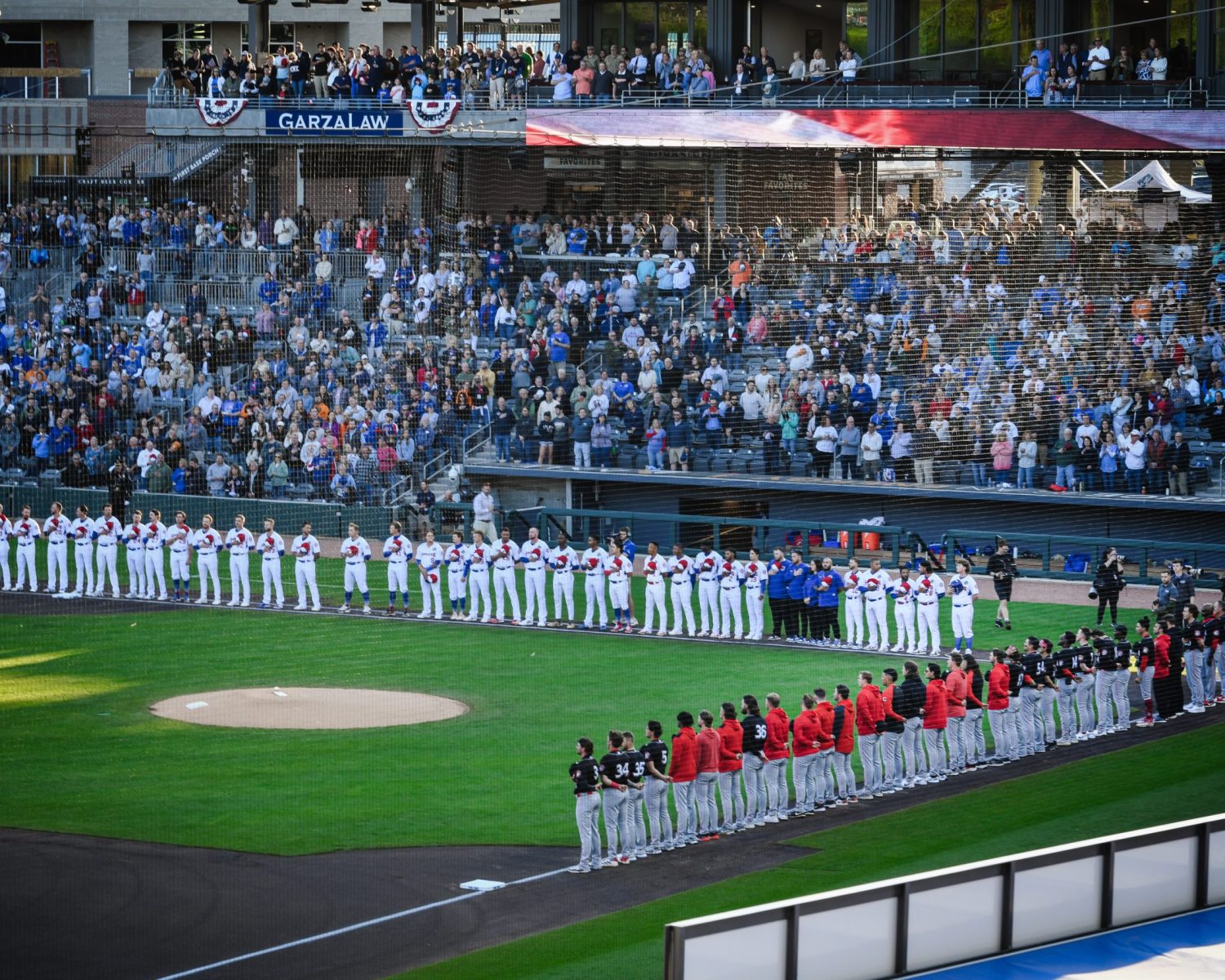 Luxury Apartments Downtown Knoxville Two baseball teams line up along the baselines during a pre-game ceremony at a stadium filled with spectators, set against the backdrop of impressive luxury downtown apartments. Knoxville Apartments For