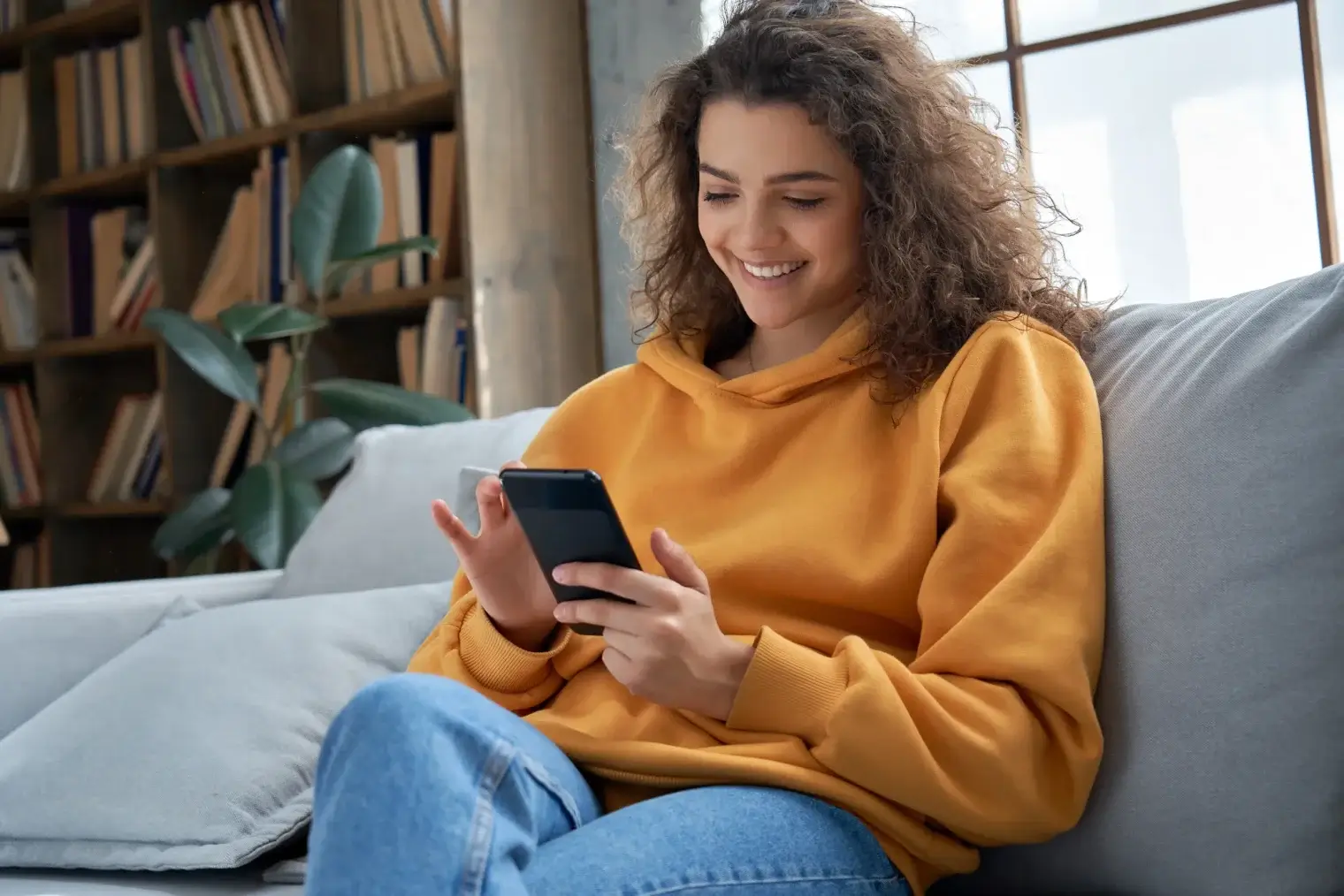A woman smiling while using her smartphone in a modern townhome at The Claire, enjoying the integrated smart tech package.