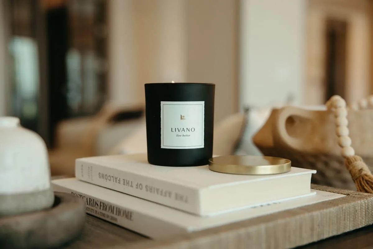 Black candle on stacked books beside a gold lid on a beige table in a softly lit room at Livano Wildwood.