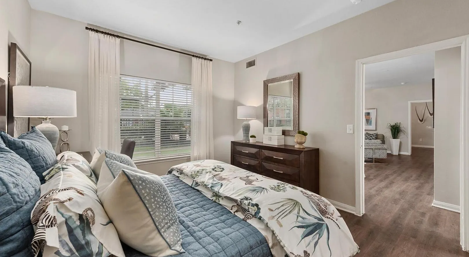 Elegant bedroom featuring luxurious bedding, natural light streaming through large windows, and a seamless transition to a cozy living area with stylish decor.
