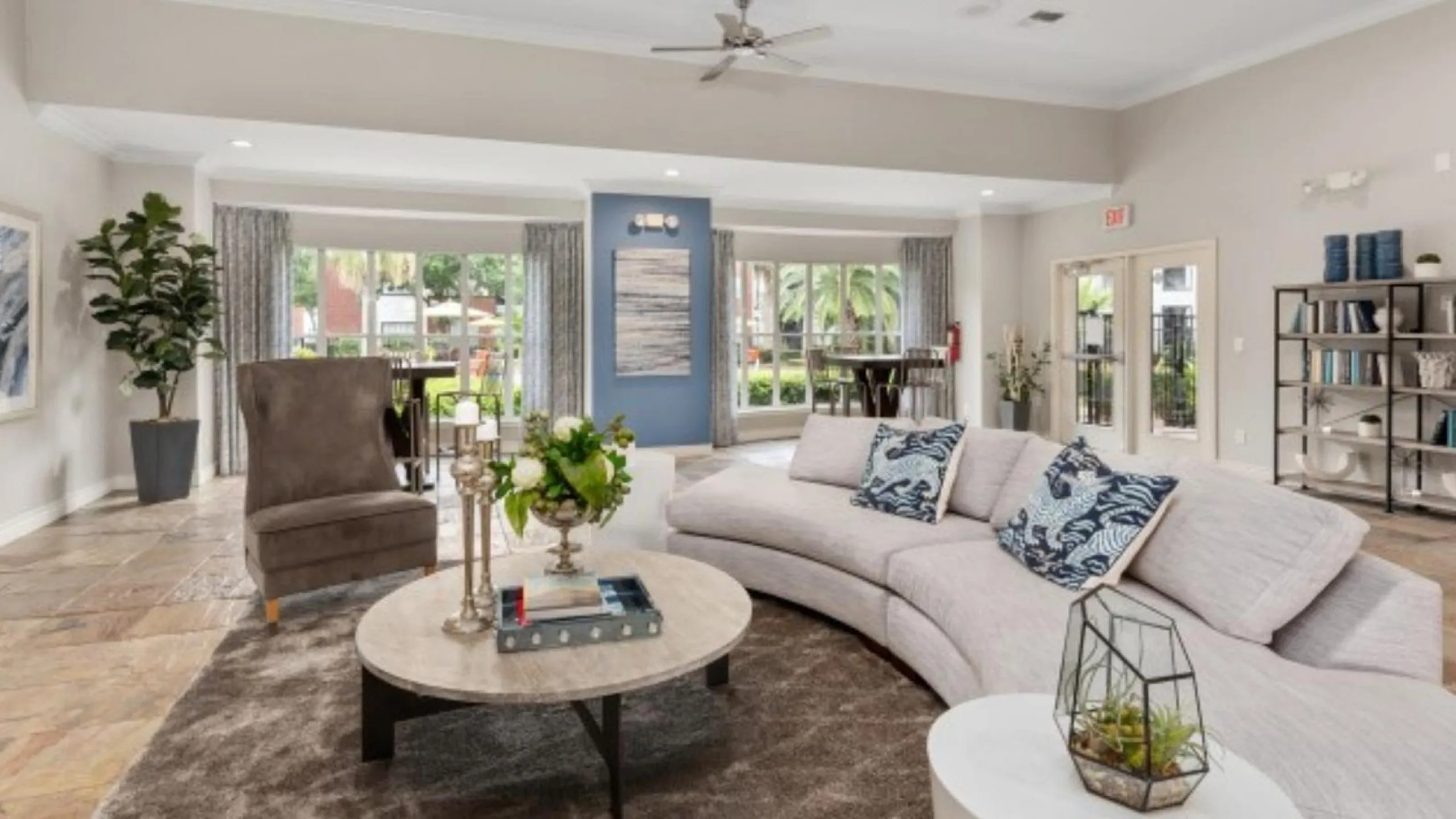 Elegant open living room with contemporary décor, featuring a plush curved sofa, stylish armchair, and floor-to-ceiling windows with a garden view.