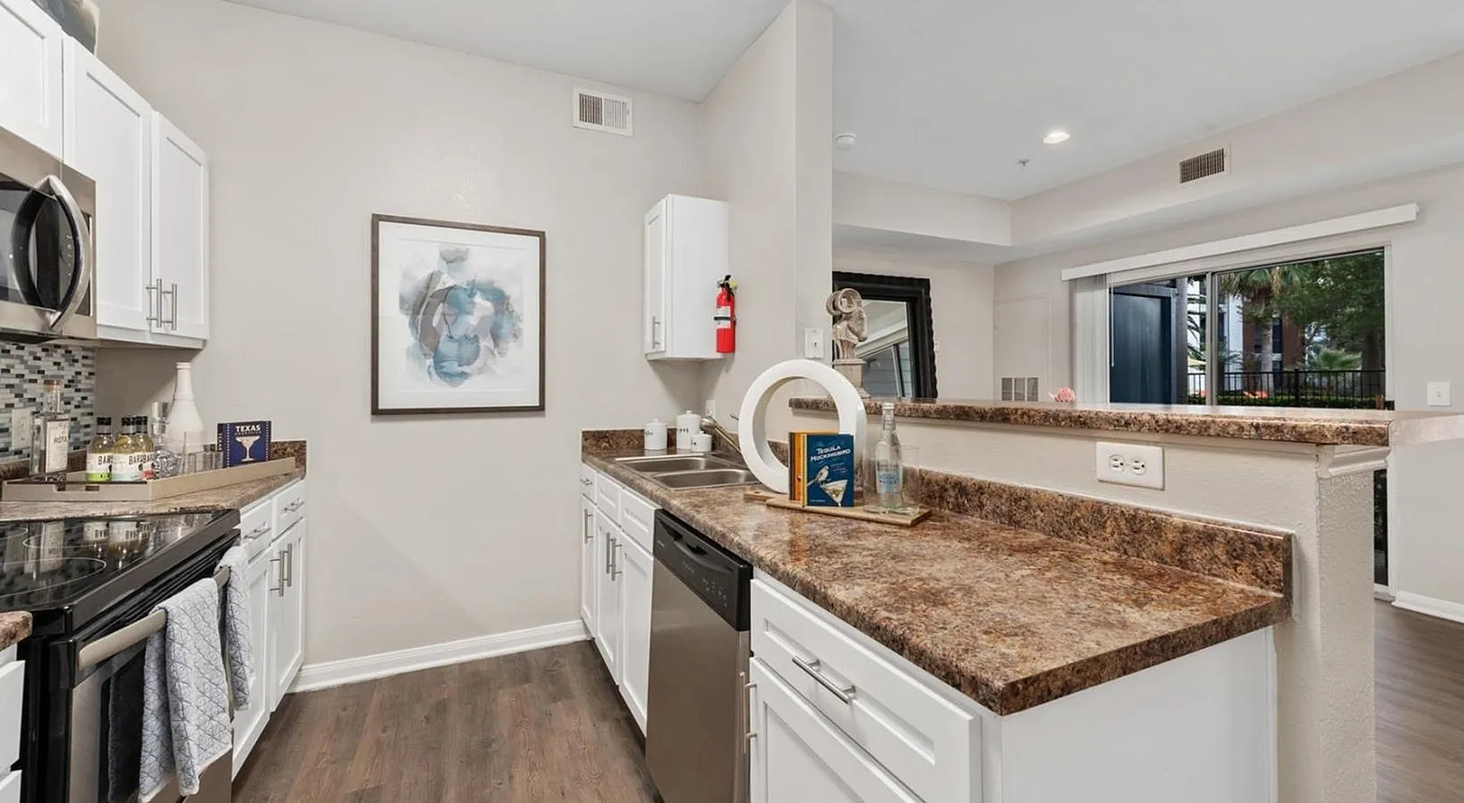 Modern kitchen with sleek white cabinetry, granite countertops, and stainless steel appliances. Bright and inviting space with a view to outdoor greenery.