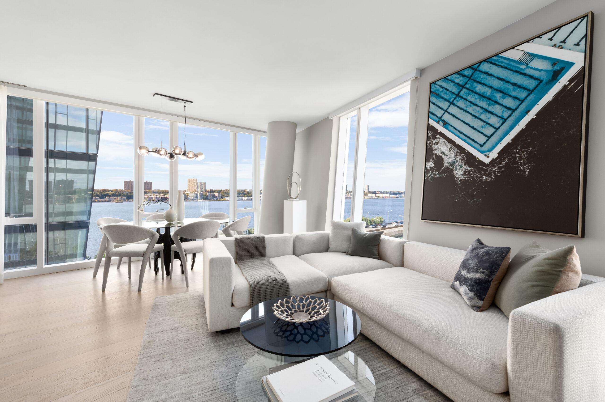 A modern living room with large windows, a sleek sofa set in neutral tones, and a striking wall painting.