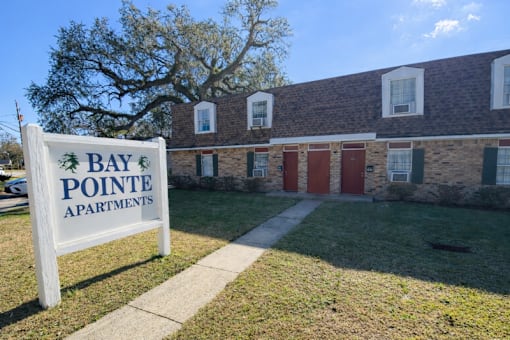 A sign for Bay Pointe Apartments stands in front of a brick building.