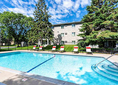 a swimming pool with chairs and a building in the background