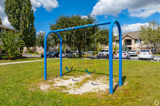 A blue swing set in a grassy area with cars and houses in the background.